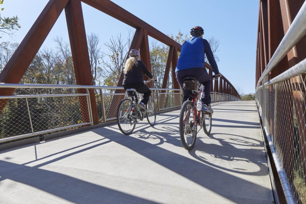 Two people bike over a bridge