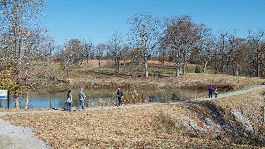 People enjoy a walking path next to a pond